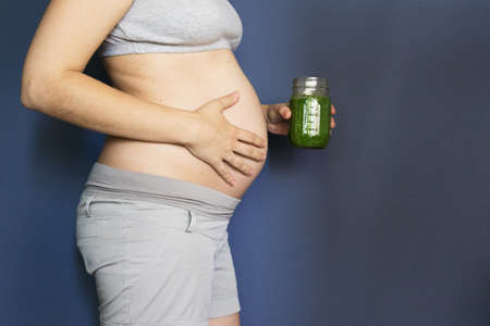 pregnancy, people and rest concept - happy pregnant african american woman drinking green vegetable...
