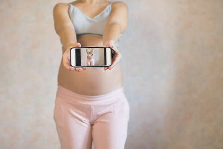 Portrait of pregnant woman taking a photo of her belly.