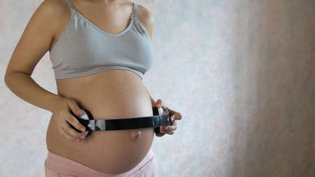 Pregnant woman holding headphone on belly on white backgroundの写真素材