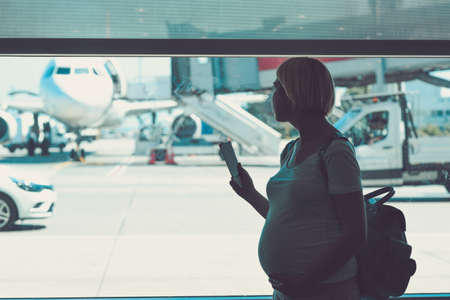 Pregnant woman is traveling by plane standing near the windowの写真素材