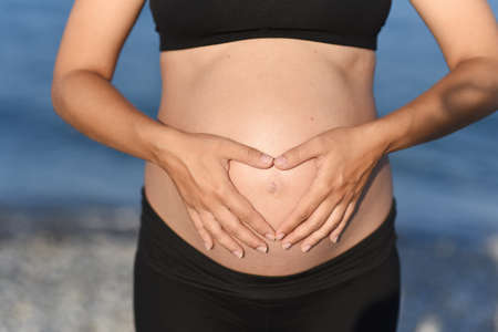 Pregnant woman beach - hands in heart shape on bellyの写真素材