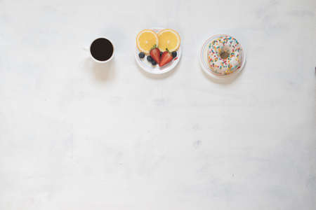 Cup of coffee and donut with curd cream decorated with crumbs of red fruit on white backgroundの写真素材