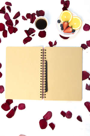 Morning Cup of coffee, empty notebook and roses flowers, fruits and donuts on white table from above. Cozy Breakfast. Flat lay style.の写真素材
