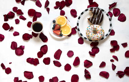 Morning Cup of coffee, empty notebook and roses flowers, fruits and donuts on white table from above. Cozy Breakfast. Flat lay style.の写真素材