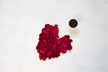 Heart from rose petals arranged in a pattern with cup of coffeeの写真素材