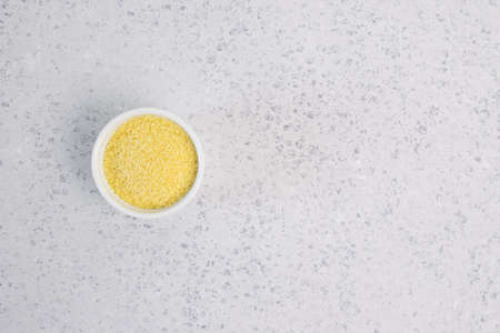 Dry couscous in white ceramic bowl isolated on grey. Spilled couscous. Healthcareの写真素材
