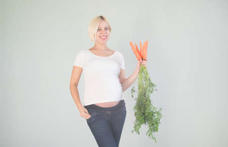 young beautiful pregnant woman with fresh carrots on light backroundの写真素材
