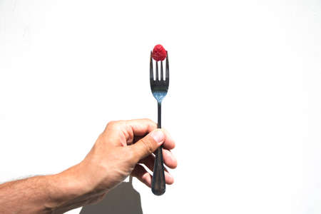male hand holding a fork with one raspberryの写真素材