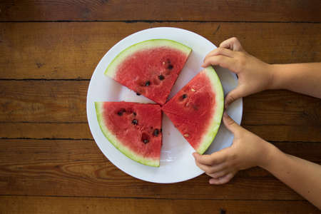 a slice of ripe watermelon in a child's hand, close up.summer timeの写真素材