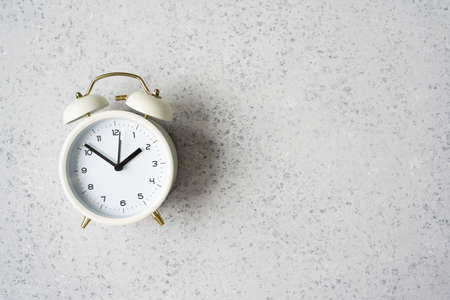 White alarm clock shows 7 after 10 on grey backround