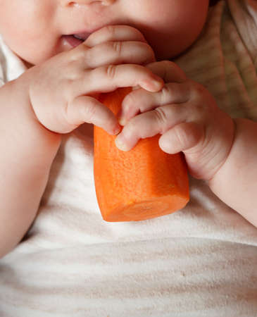 Happy baby girl trying her first vegetable solid food, a carrot.の写真素材