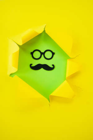ripped yellow paper against a green background with mustache and glass in itの写真素材