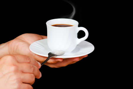 Hands with a cup of coffee with steam on a black backgroundの写真素材