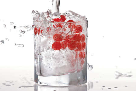 Glass of water, ice and red cranberries with splash on a white backgroundの写真素材
