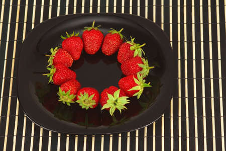 Black dish with ripe fresh strawberries on a white backgroundの写真素材