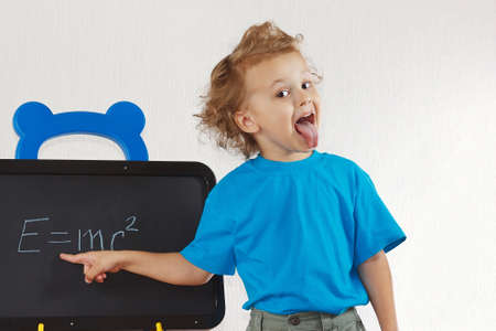 Little boy shows tongue like Einstein near formula on a blackboard