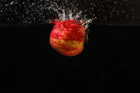 Fresh apple falling into the water with a splash on a dark background closeupの写真素材