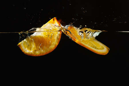 Two segments of fresh orange falling into the water with a splash on a black background