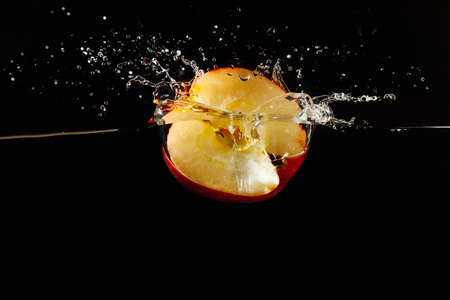 Halved apple falling into the water with a splash on a dark background closeup