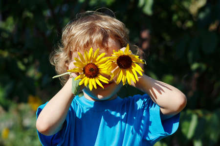 Young blond boy playing with sunflowers outdoors on a sunny dayの写真素材