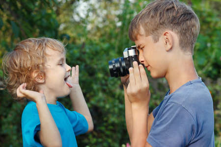 Young photographer with a camera shoots her little brother outdoorsの写真素材