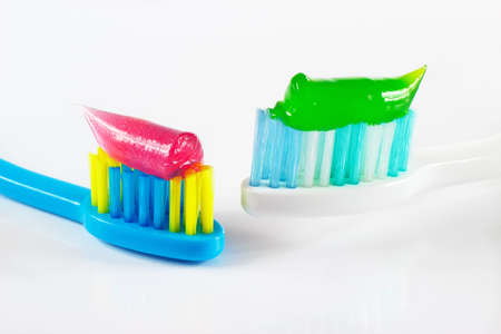 White and blue toothbrushes with pink and green toothpaste on white backgroundの写真素材