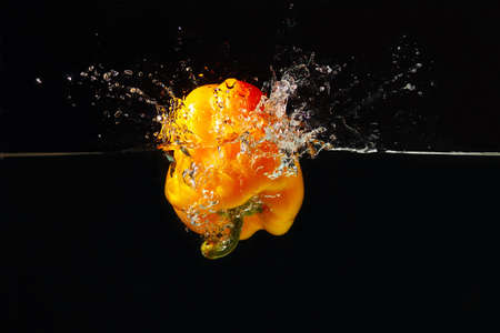 Fresh yellow bellpepper falling into the water with a splash on a black background 