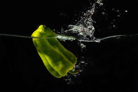 Green bellpepper falling into the water with a splash on a black background closeupの写真素材