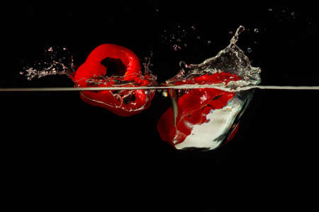 Slices of red pepper falling into the water with a splash on a black background 