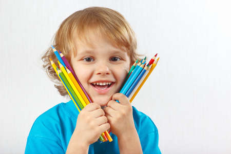 Little smiling boy holds color pencils on a white backgroundの写真素材