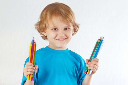 Young blond boy holds color pencils on a white backgroundの写真素材