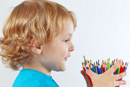 Little child looks on color pencils on a white backgroundの写真素材