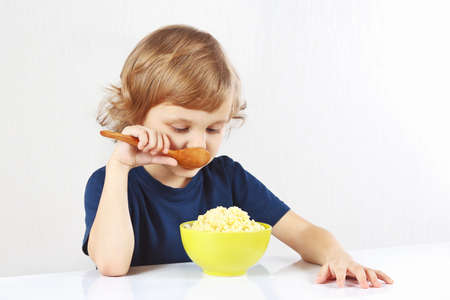 Little blonde boy eating a millet porridge on white backgroundの写真素材