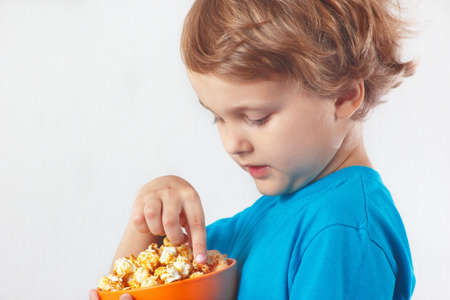 Beautiful blonde boy eating popcorn on a white backgroundの写真素材