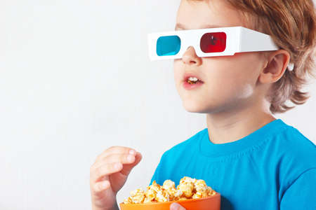 Young blonde boy in stereo glasses eating popcorn on white backgroundの写真素材
