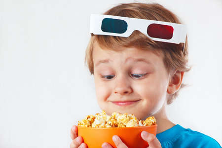 Little funny boy in 3D glasses with bowl of popcorn on white backgroundの写真素材