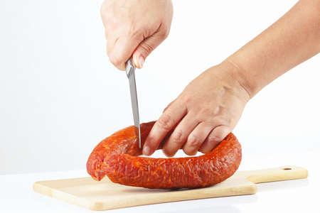 Female hand with a knife sliced smoked sausage on a white background