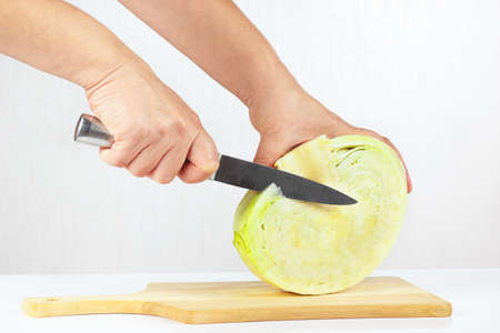 Hands cuts fresh cabbage on a wooden cutting board closeupの写真素材