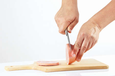 Hands with a knife sliced sausage on a wooden cutting board closeupの写真素材
