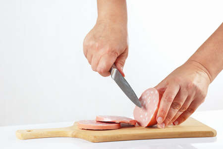 Female hands sliced sausage on a wooden cutting board closeupの写真素材