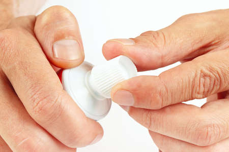 Hands open tube of toothpaste on a white 
