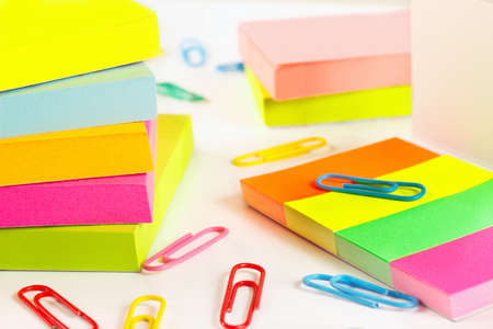 Paperclips and multicolored stickers on white desktop close up