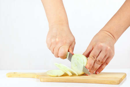 Hands chops raw onion on a cutting board close upの写真素材