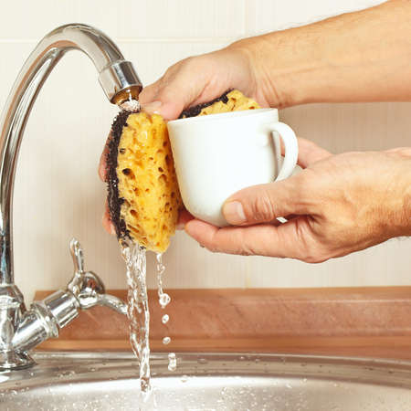 Hands wash the coffee cup under running water in the kitchenの写真素材