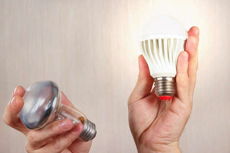 Hands compared incandescent bulb and glowing ecofriendly led lamp on a light wood backgroundの写真素材