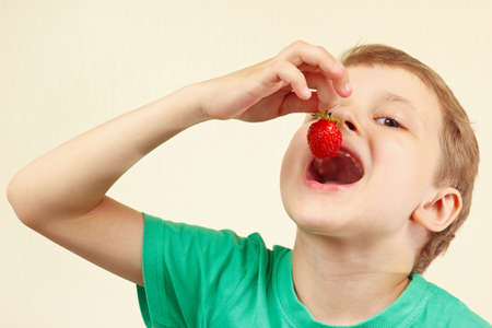 Young funny boy eating a fresh ripe strawberryの写真素材
