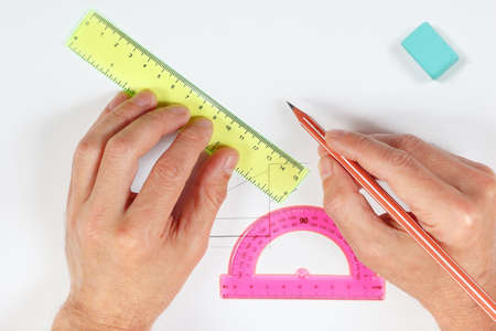 Hands making a drawing with pencil and ruler on a white sheet of paper