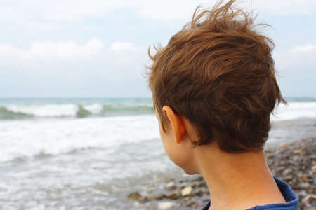 Little boy on the shore watching the sea wavesの写真素材