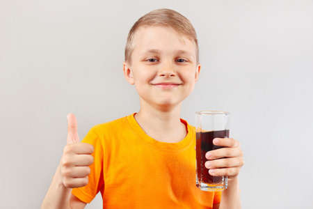 Little smiling boy with a glass of fresh colaの写真素材