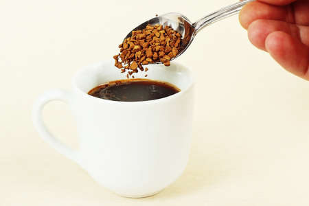 Hand pours granulated coffee from a spoon in a coffee cup, gently tonedの写真素材
